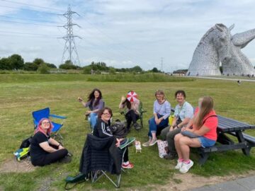 talk and sign group sitting on the grass, the kelpies are in the background on the right.