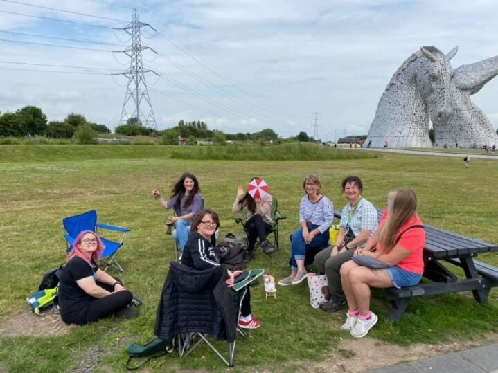 talk and sign group sitting on the grass, the kelpies are in the background on the right.