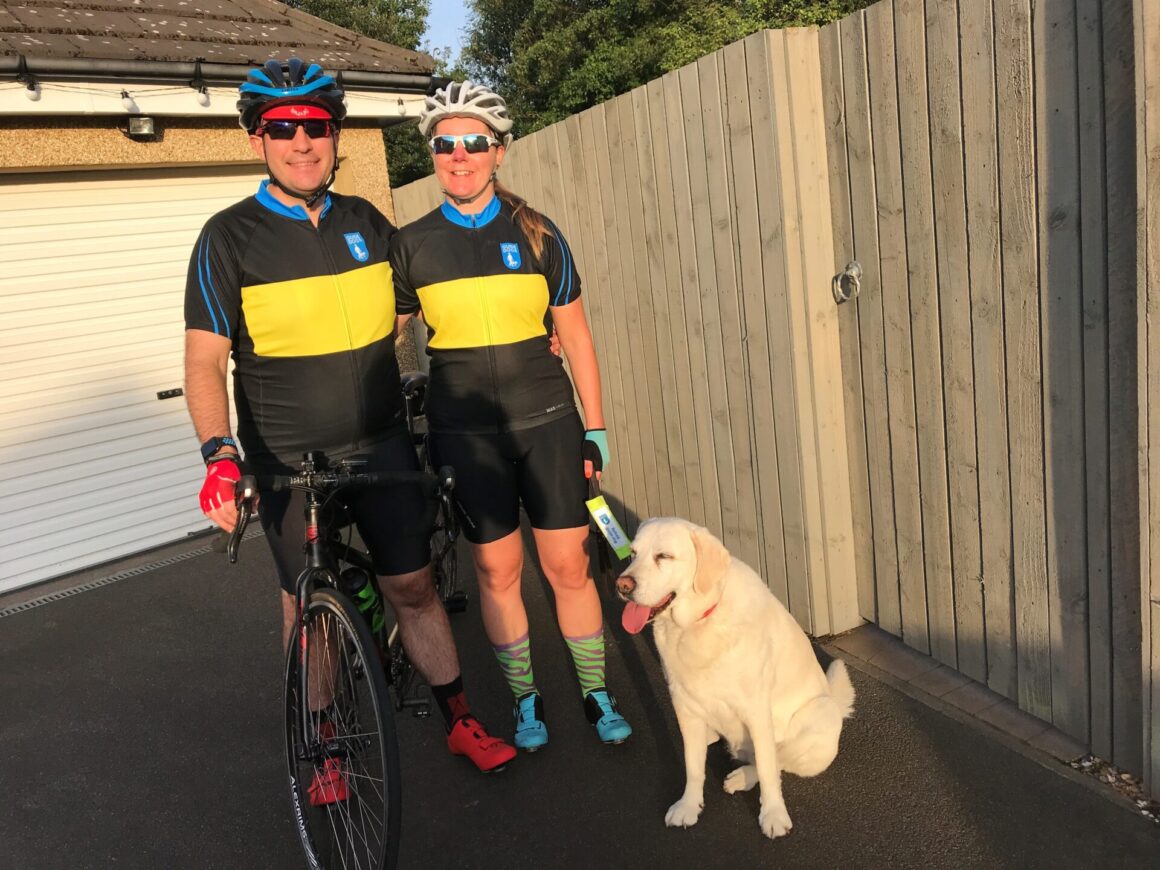 Laura and Joe with their tandem and wearing their Guide Dogs tops. Pixie watches on