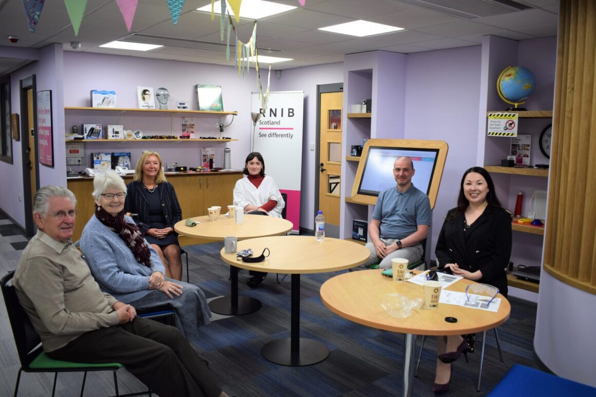 Monica Lennon MSP seated in our Tech Hub with Ian and Cathy, Jacquie winning, Sara Burns and our BSL interpreter