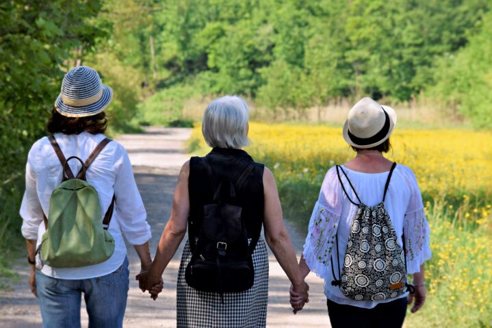 three older women holding hands and walking in the countryside