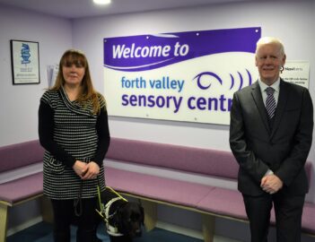Laura Cluxton, Guide Dog Sadie and Councillor Robert Mooney stand in front of Forth Valley Sensory Centre sign