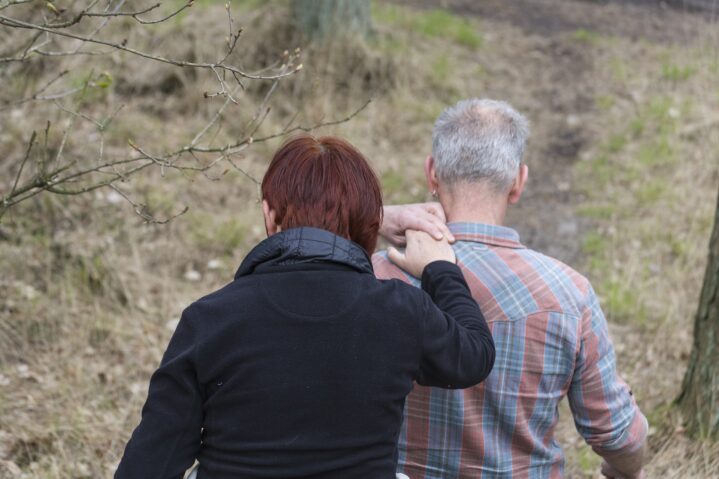 Two people. One has their hand on the shoulder of the sighted guide in front