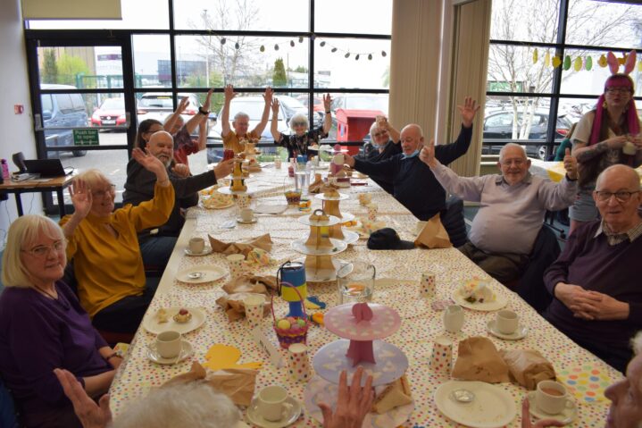 Deaf OAP Group table with 12 people waving and smiling at the camera