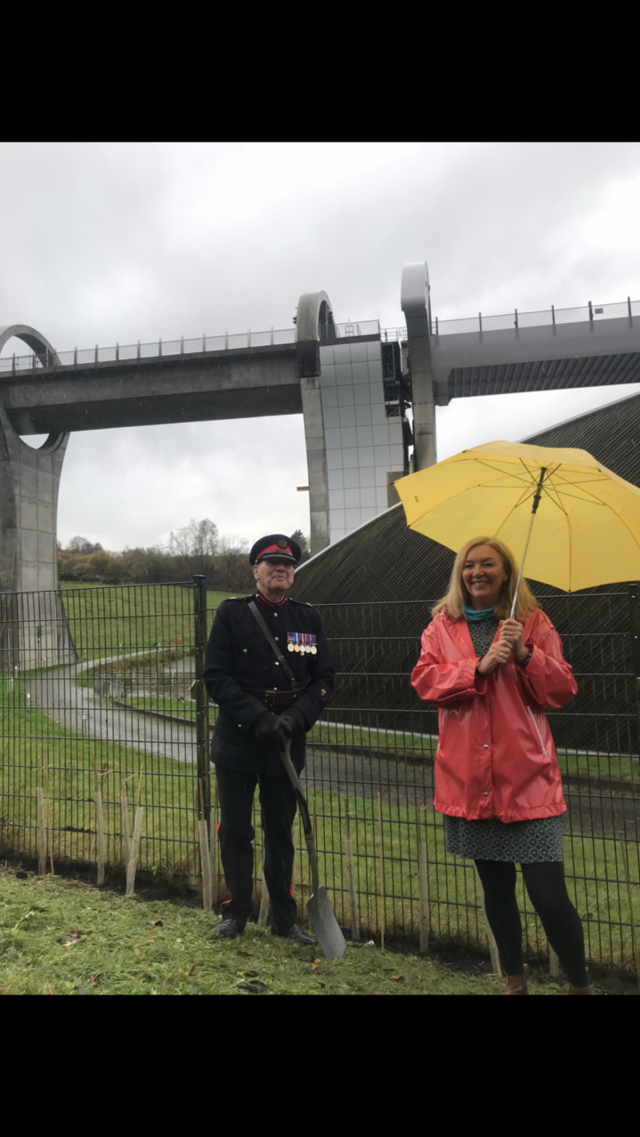 Jacquie Winning and Colonel Alastair Campbell DL, Vice Lord Lieutenant for Stirling and Falkirk stand next to the planted trees. The Falkirk Wheel is in the background